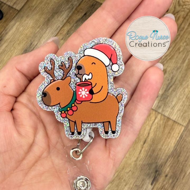 Capybara Riding a Reindeer Holding Hot Chocolate and wearing a Santa Hat Retractable Badge Reel, UV Printed on Silver Glitter Acrylic