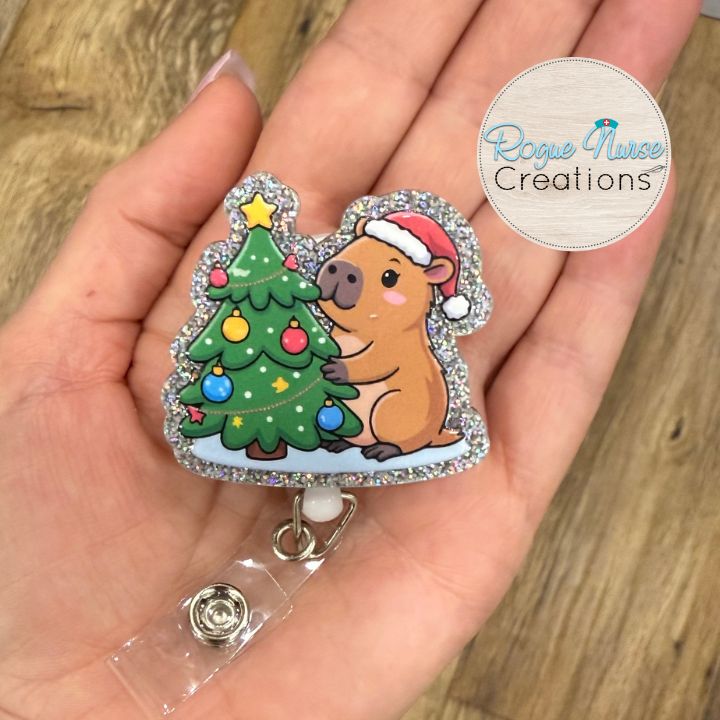 Capybara decorating a Christmas Tree Wearing a Santa Hat Retractable Badge Reel, UV Printed on Silver Glitter Acrylic